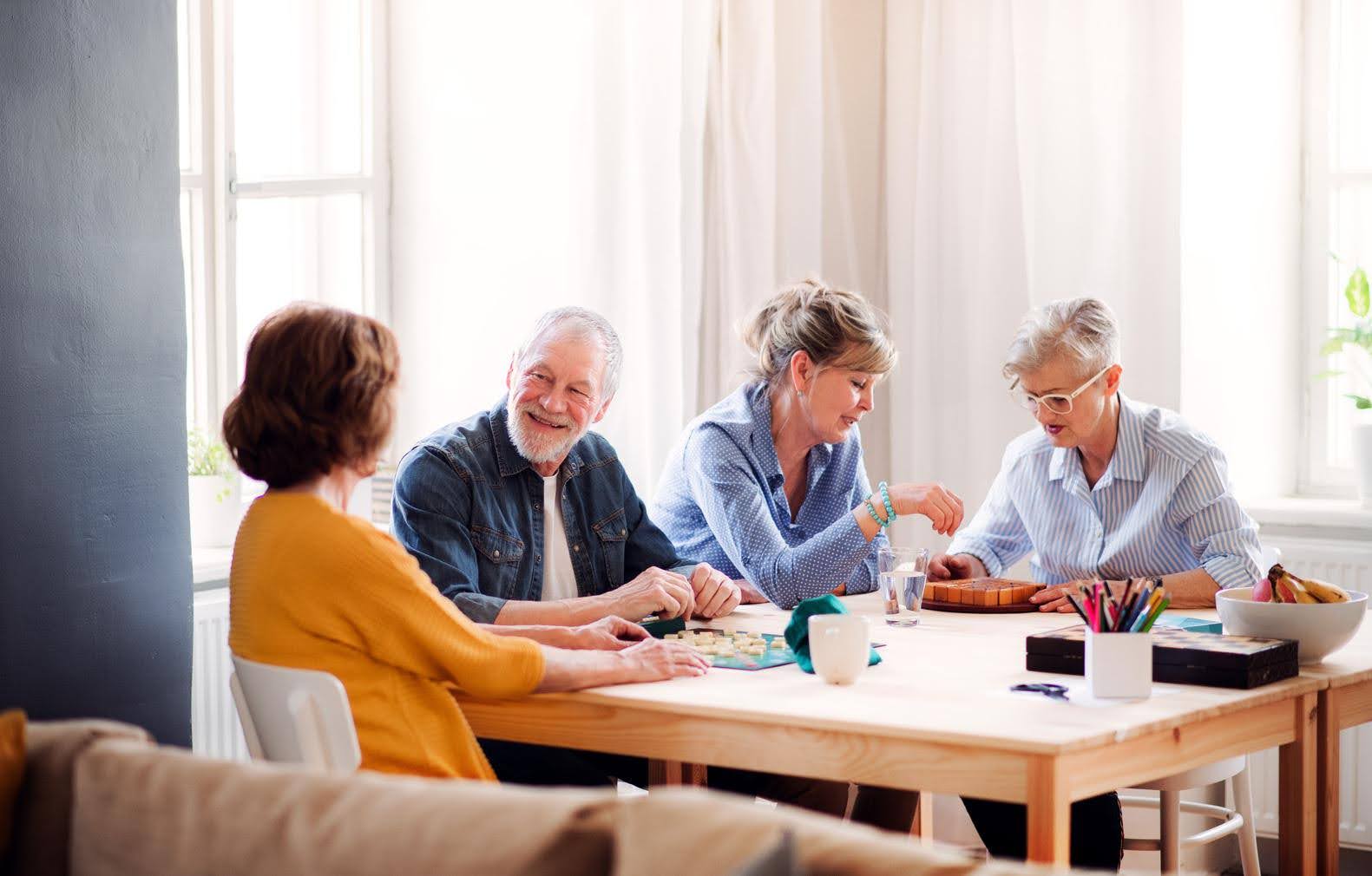 Group of seniors sitting around a table in a bright room, enjoying activities together, representing facility requirements for opening a senior center.