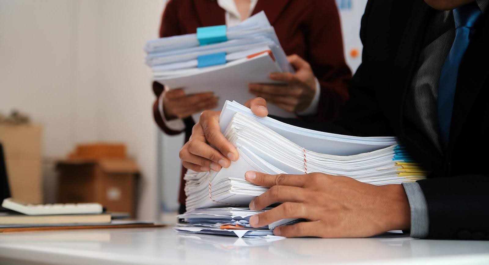 Healthcare inspectors reviewing stacks of documents during a site visit to ensure compliance and proper licensing in healthcare facilities.