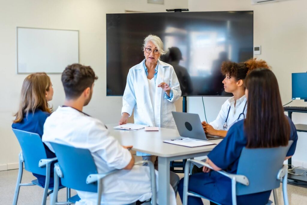 Healthcare staff receiving training from a senior instructor in a home health agency meeting to maintain quality and compliance standards.