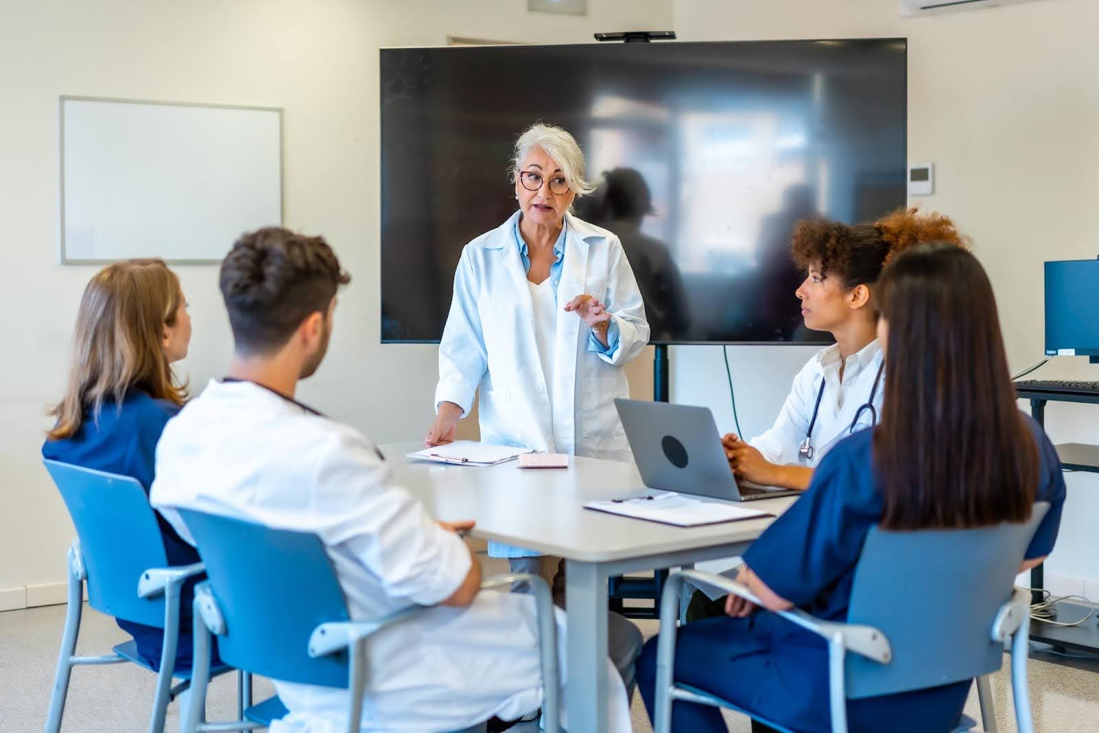 Healthcare staff receiving training from a senior instructor in a home health agency meeting to maintain quality and compliance standards.