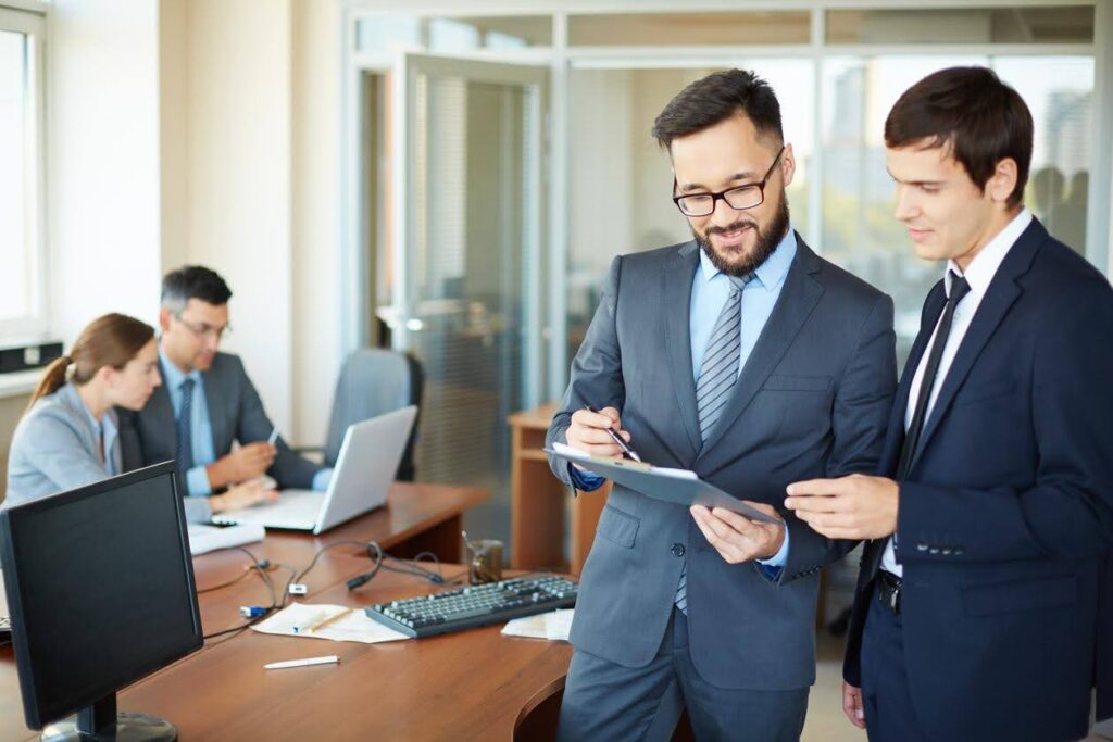 Business professionals reviewing documents in an office while discussing whether to Outsource licensing support, highlighting consulting services from CTK Advisors.